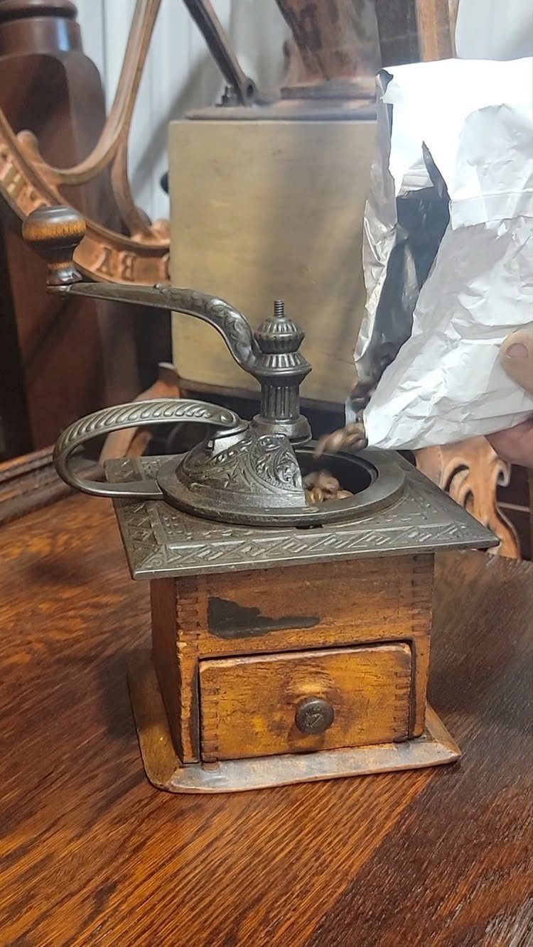 17 Antique Coffee Decor Ideas for Your Kitchen or Nook 14 Vintage manual coffee grinder on a wooden table with beans being poured in.