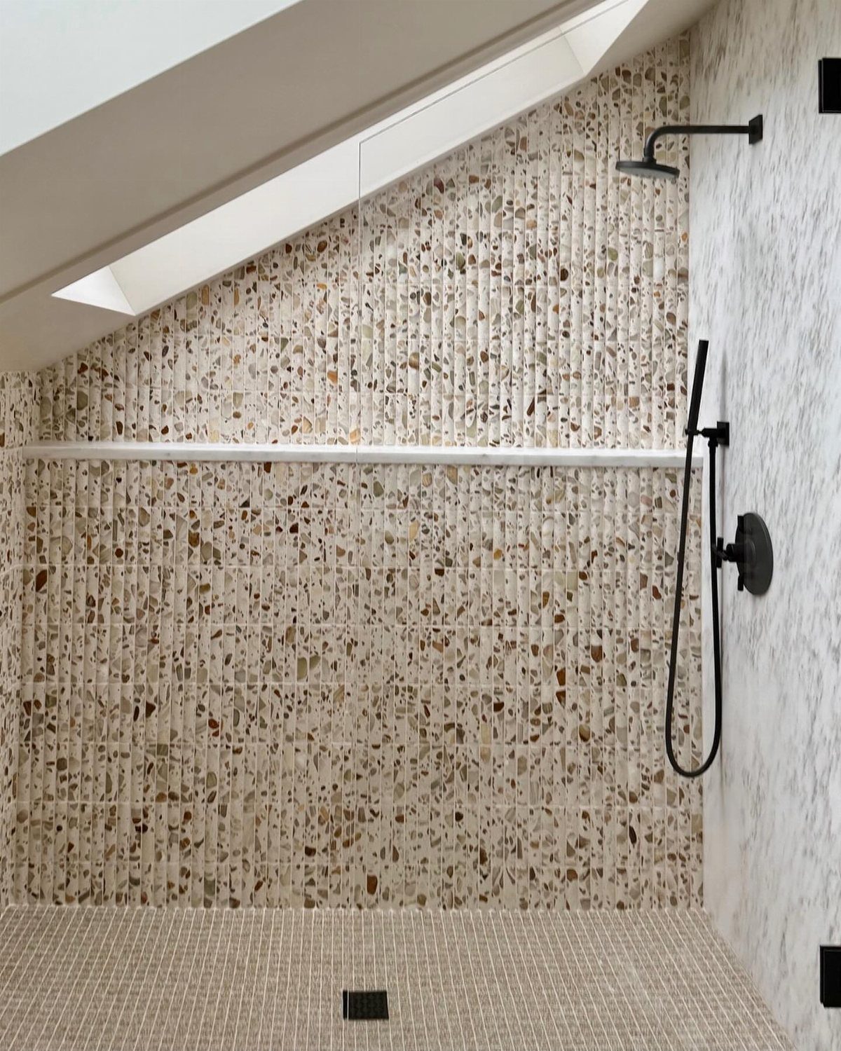 Fluted terrazzo wall tiles in a shower with black fixtures and mosaic flooring.