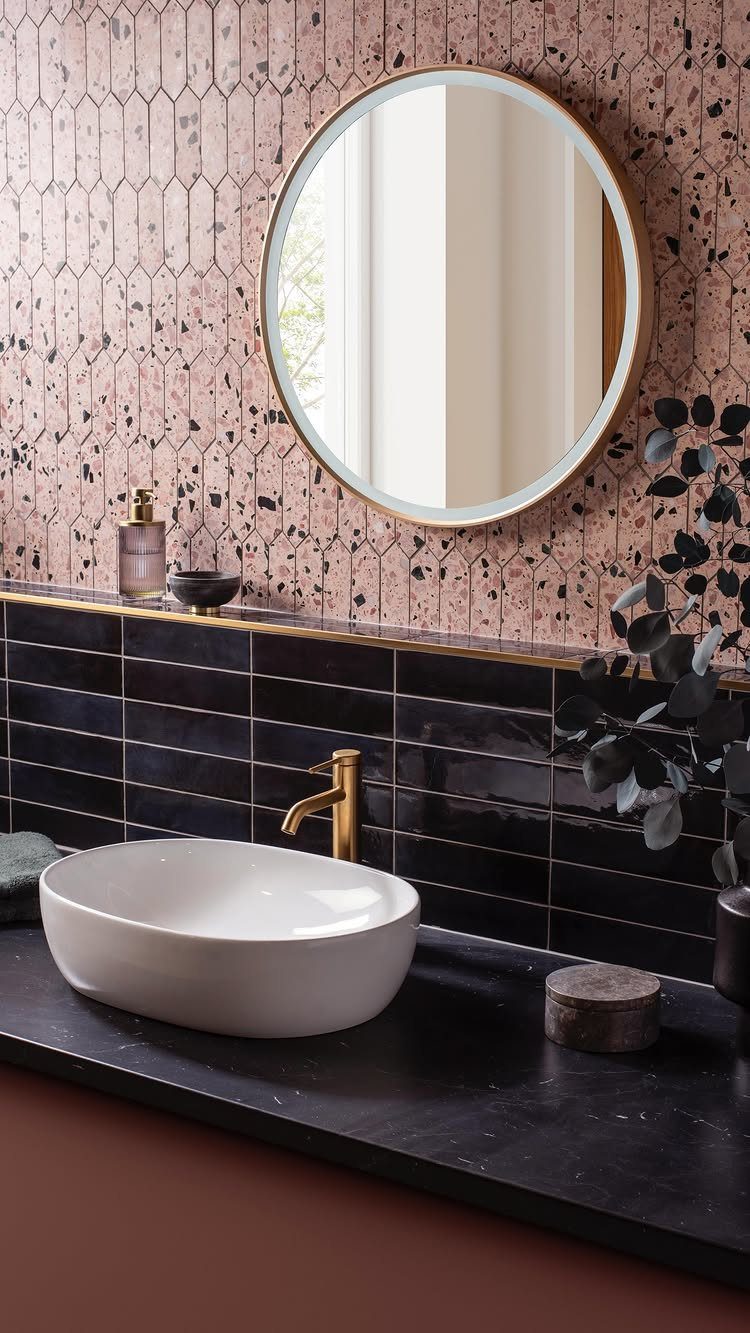 Pink terrazzo patterned wall with a round gold mirror and white vessel sink.