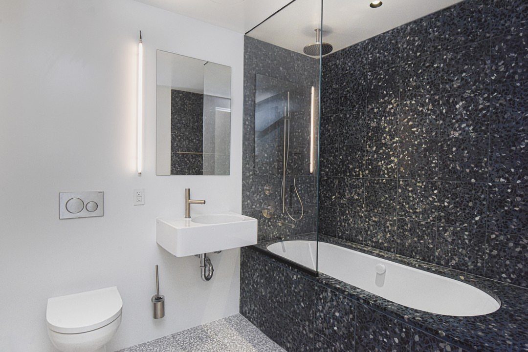 Dark grey terrazzo tiled accent wall and bathtub surround in a modern white bathroom