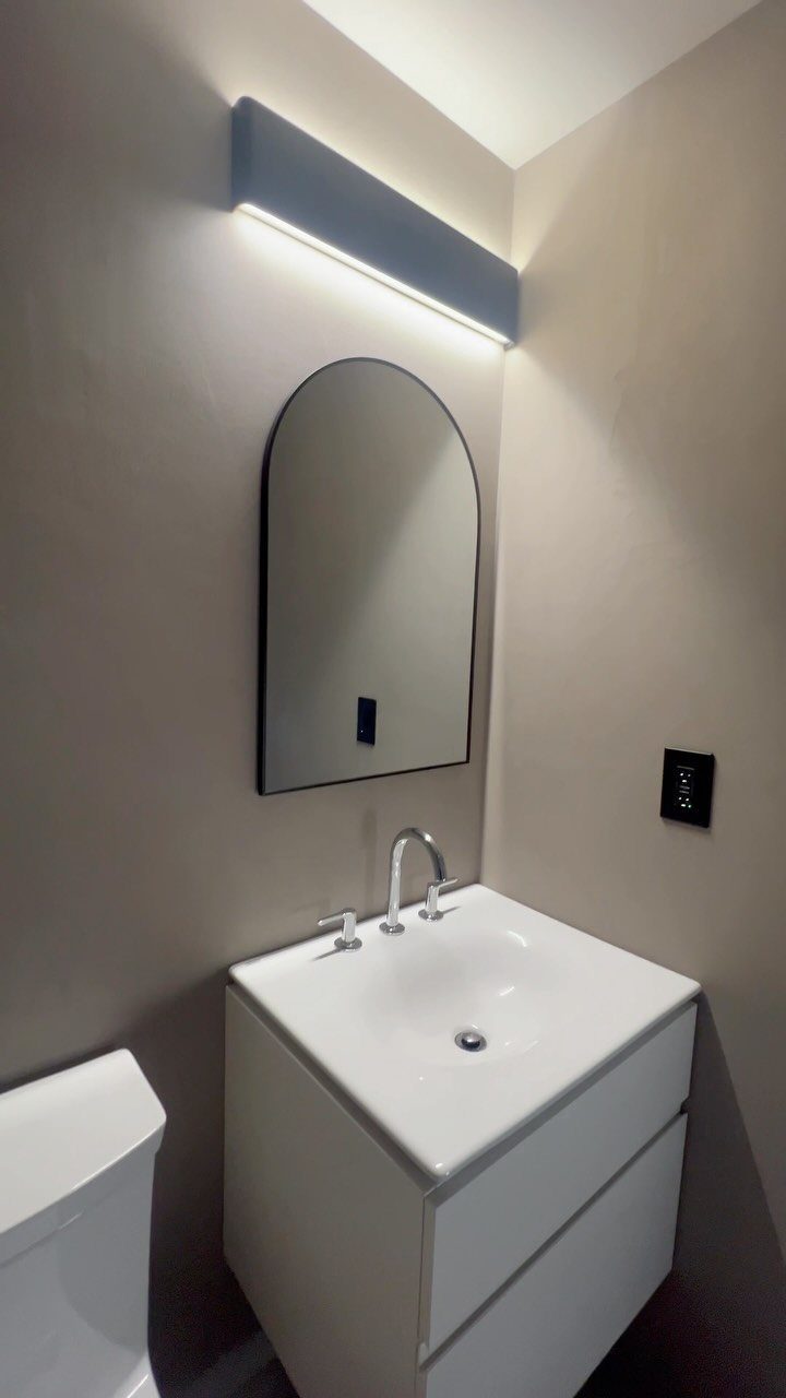 White flat-front vanity with integrated sink and arched black-framed mirror in beige bathroom.