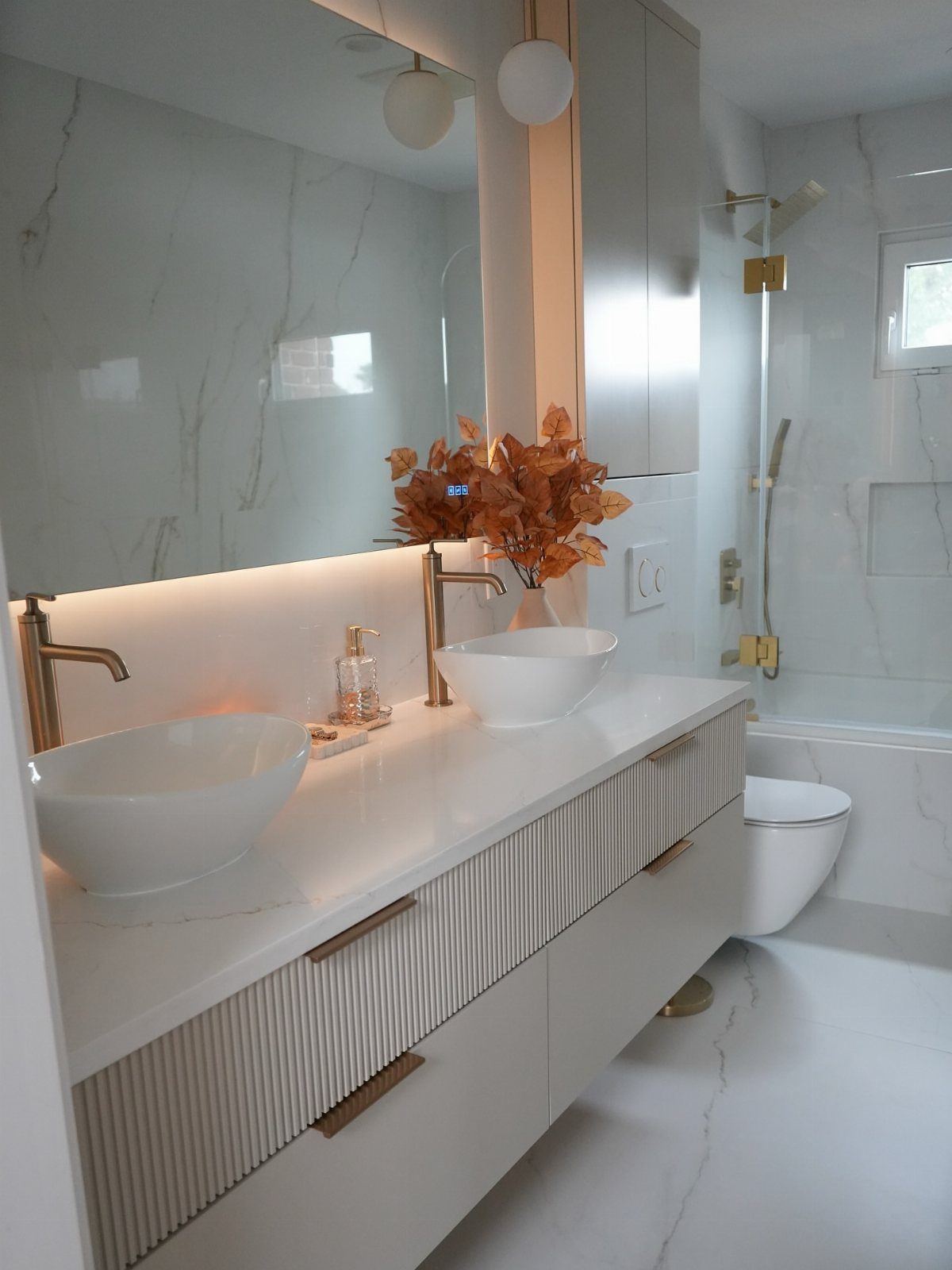 White floating vanity with fluted fronts, gold fixtures, and two white vessel sinks.