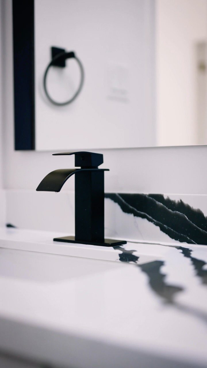 Matte black faucet on a white marble countertop with black veining.