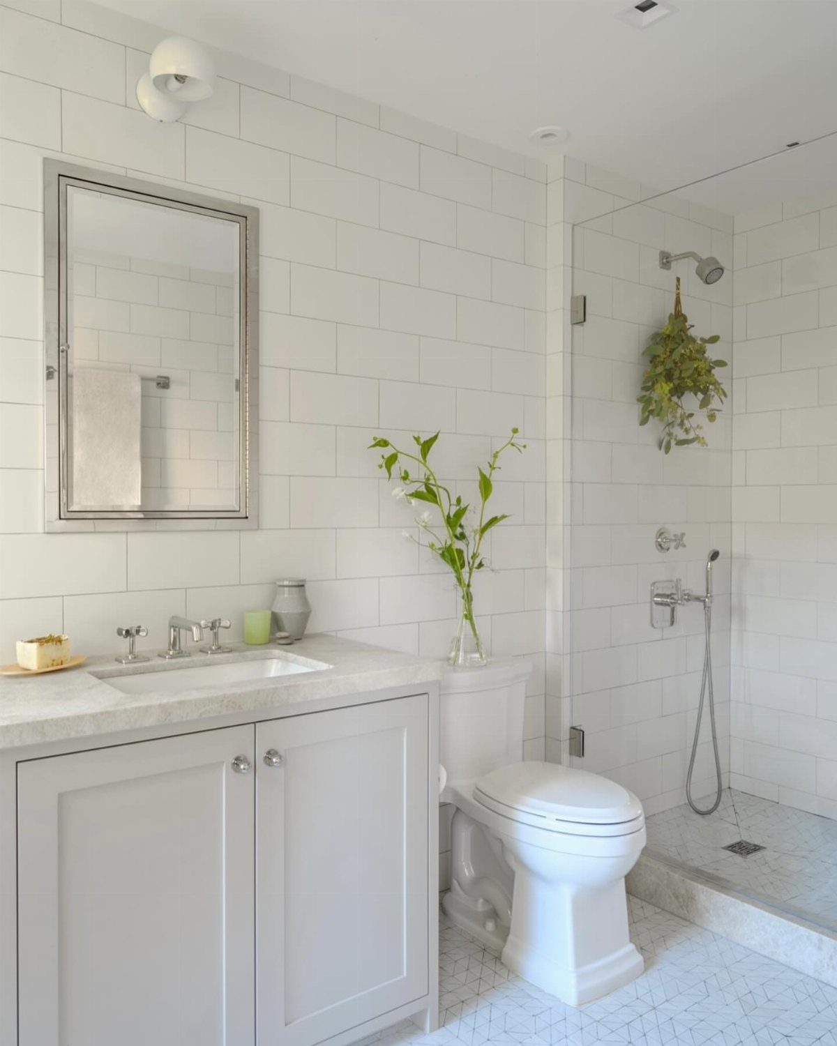 White shaker-style vanity and toilet in a bright bathroom with white subway tiles.