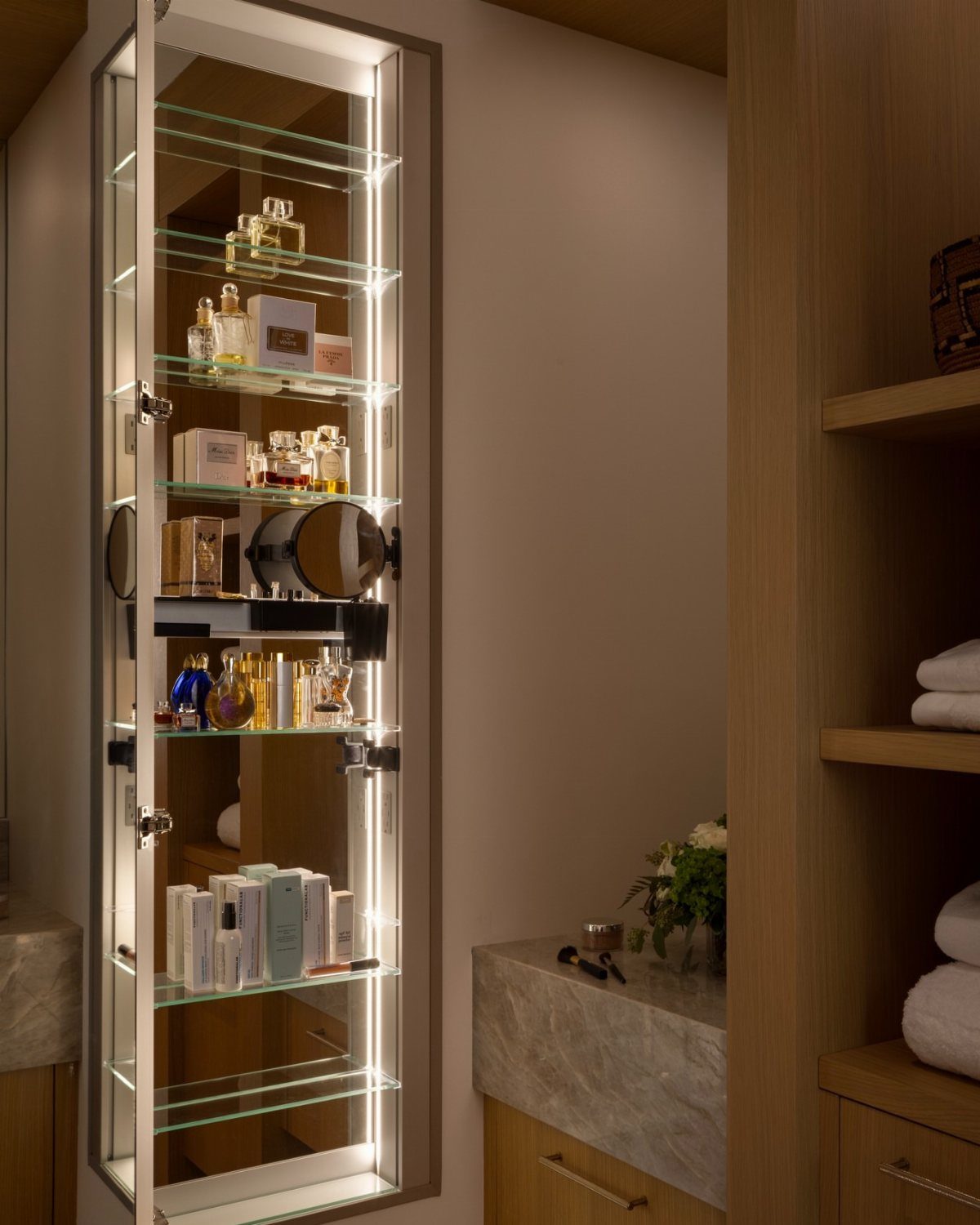 Open recessed shaving cabinet with integrated LED lighting and glass shelves holding perfumes.