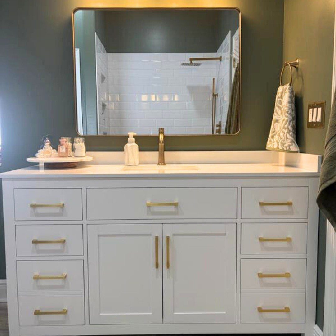 Single-basin white vanity with gold hardware and a gold-framed mirror on green walls.
