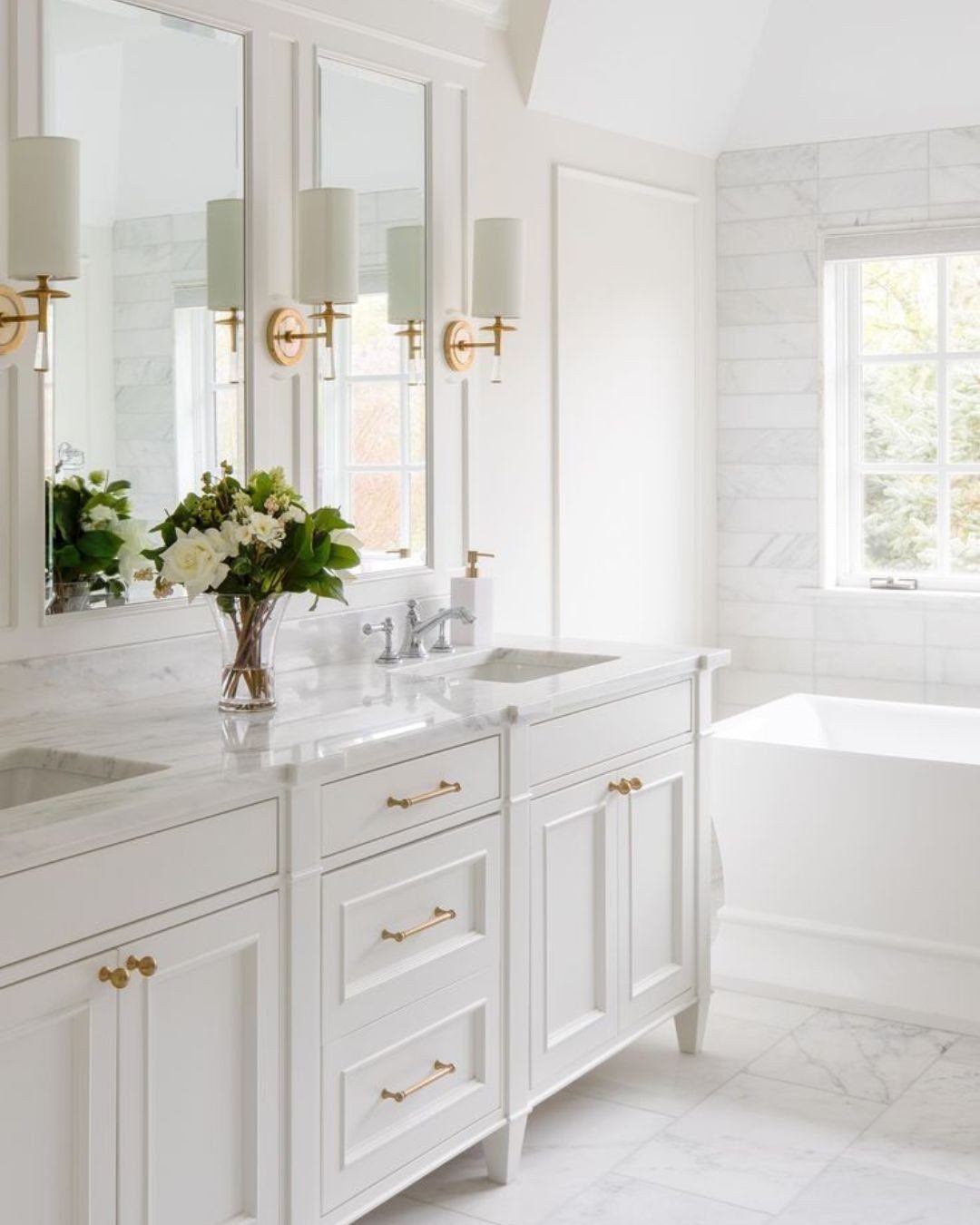 White shaker vanity with gold metallic fixtures and marble countertop in a bright bathroom.