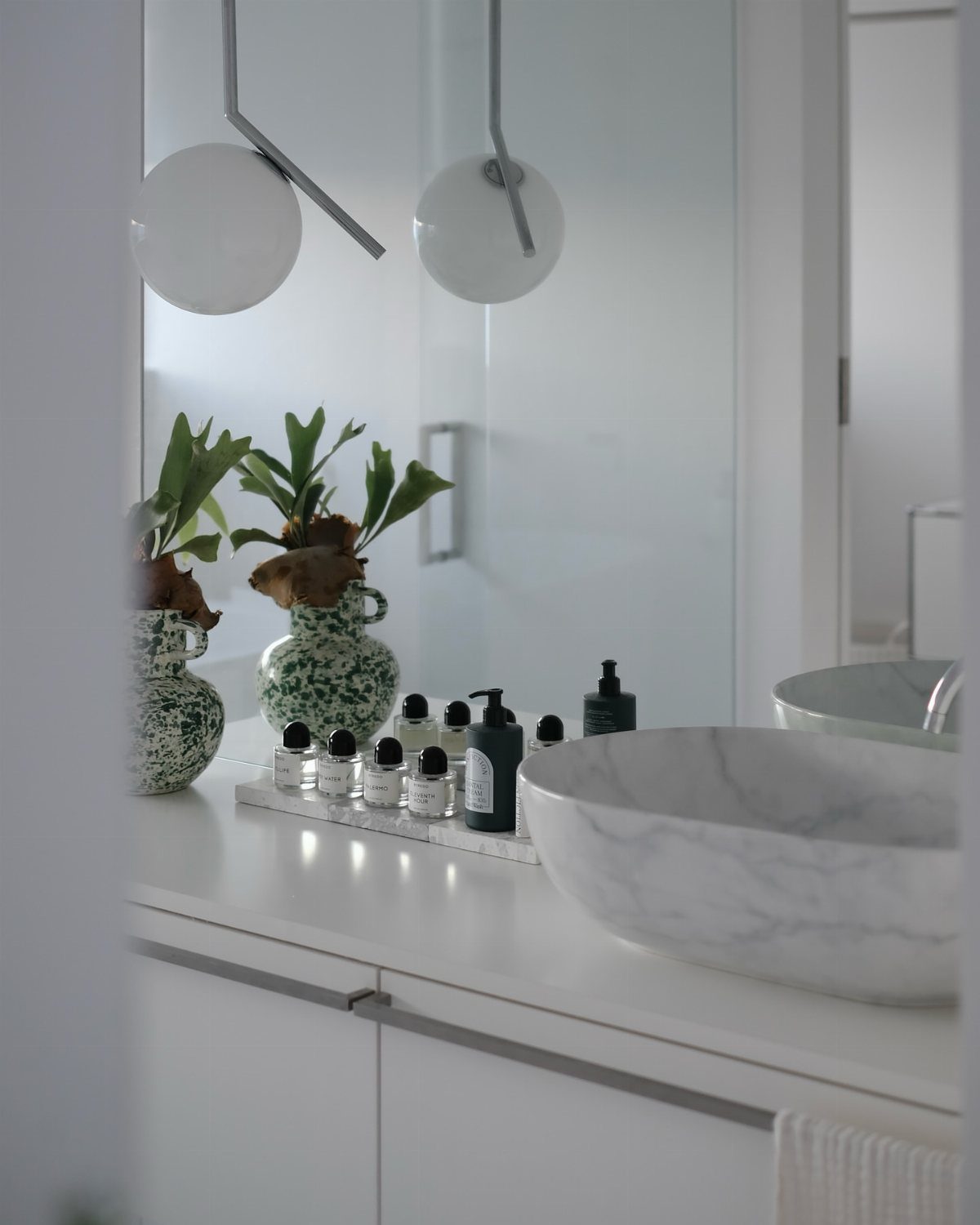 White bathroom vanity with a marble vessel sink and minimalist white pendant lights.