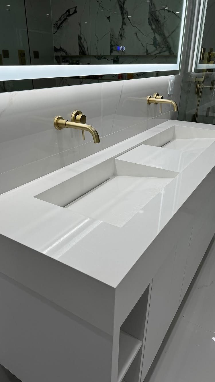 White bathroom vanity with integrated white countertop and gold wall-mounted faucets.