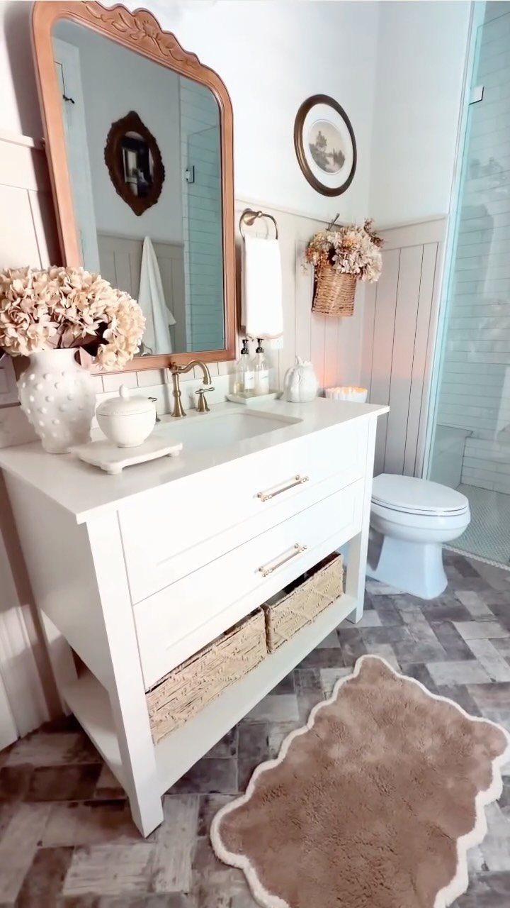 White bathroom vanity with gold hardware, ornate mirror, and brown scalloped rug.