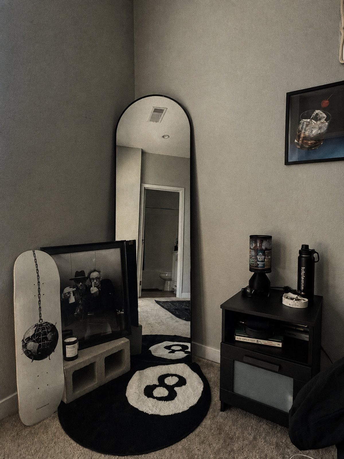 Arched full-length mirror with black frame leaning against a grey bedroom wall.