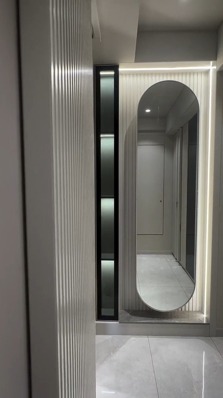 Oval full length mirror with backlighting on a white fluted wall panel.