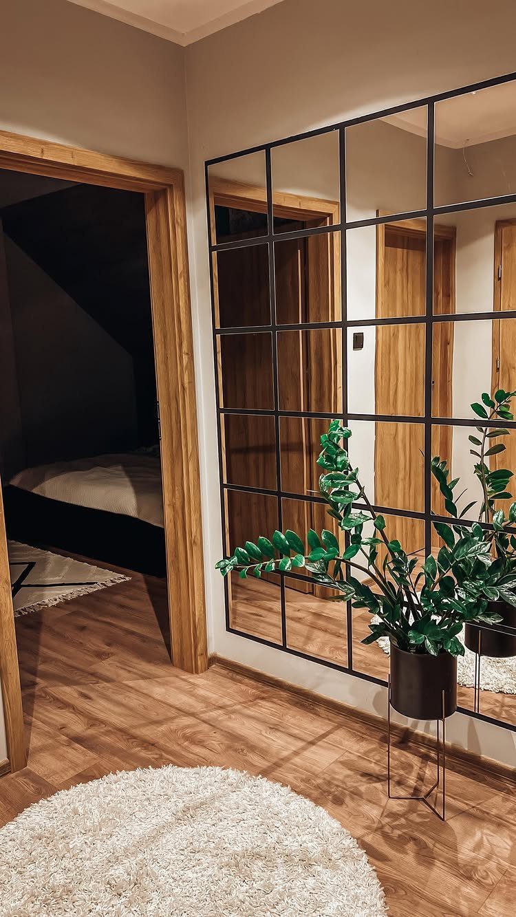 Full length black grid wall mirror in a bedroom with wooden floors and plant