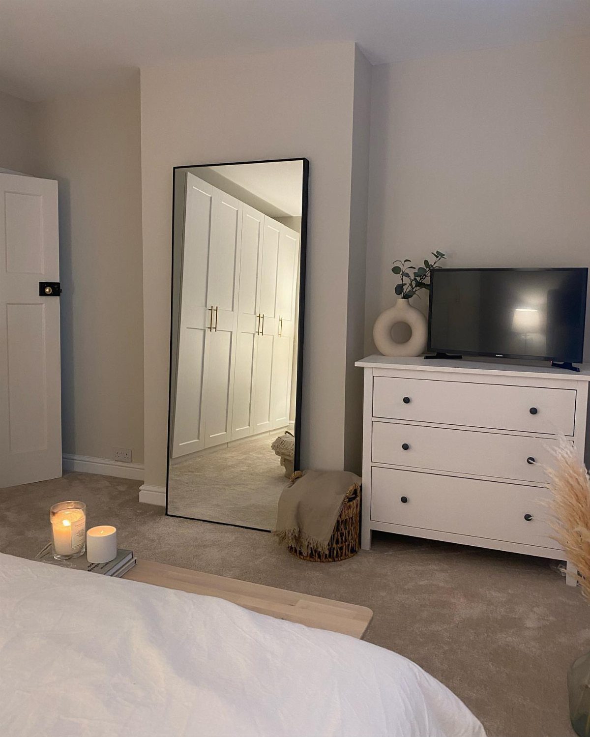 Full-length rectangular mirror with black frame leaning against a white bedroom wall