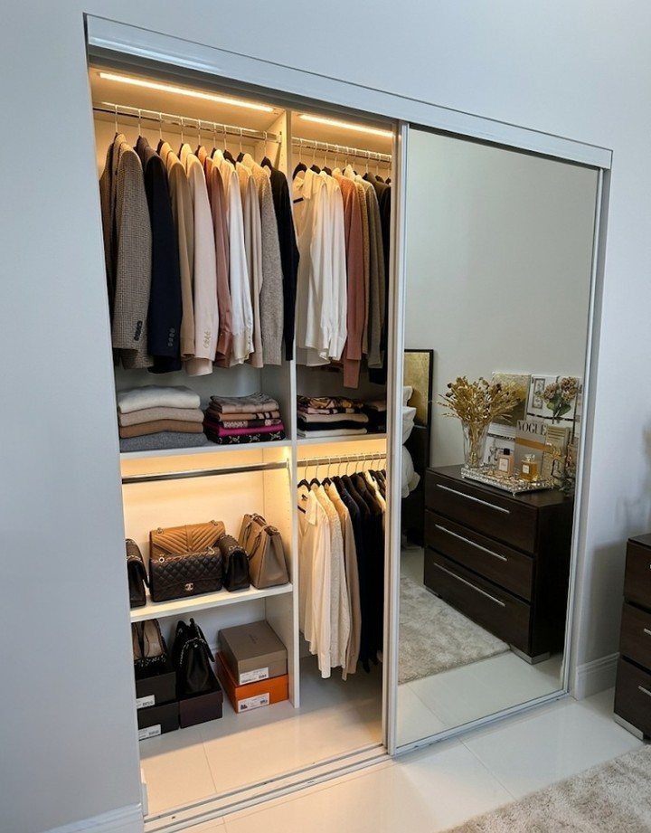Full-length mirrored sliding closet door next to an open wardrobe with organized clothing.