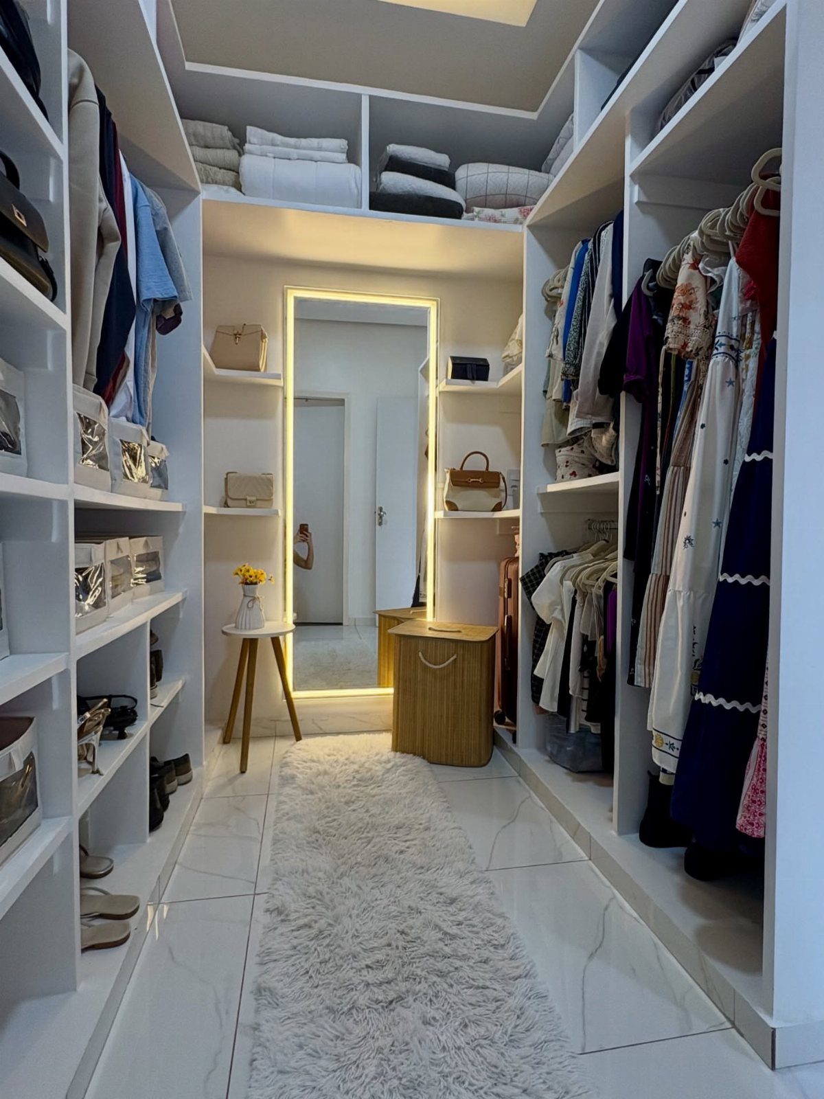 Full-length backlit mirror at the end of a white walk-in closet with clothing