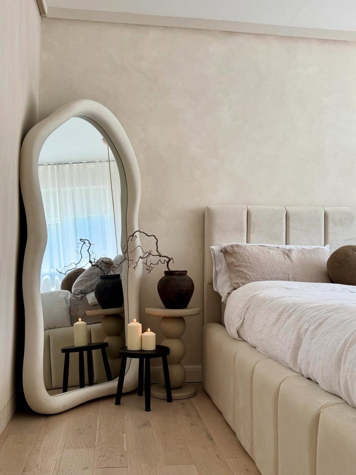 Wavy white full-length mirror leaning against a beige wall in a modern bedroom