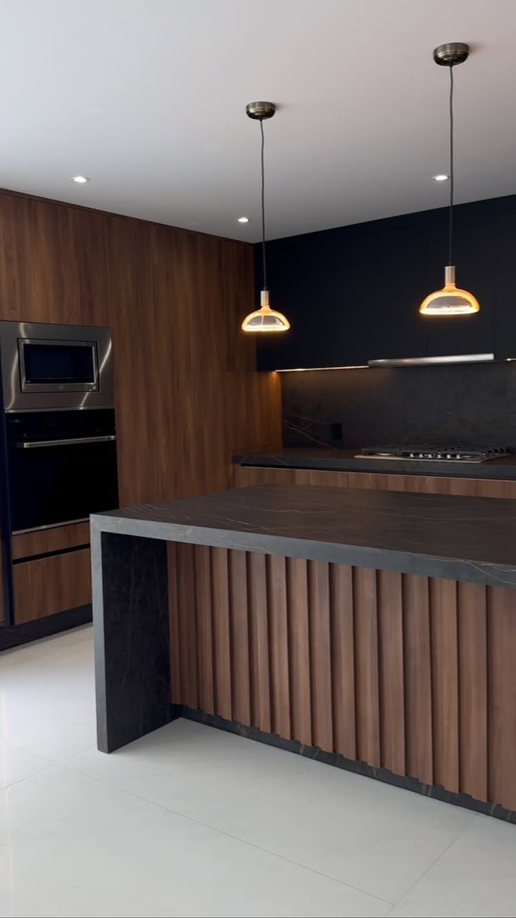 Modern kitchen with walnut wood slats, black walls, and a dark grey island.