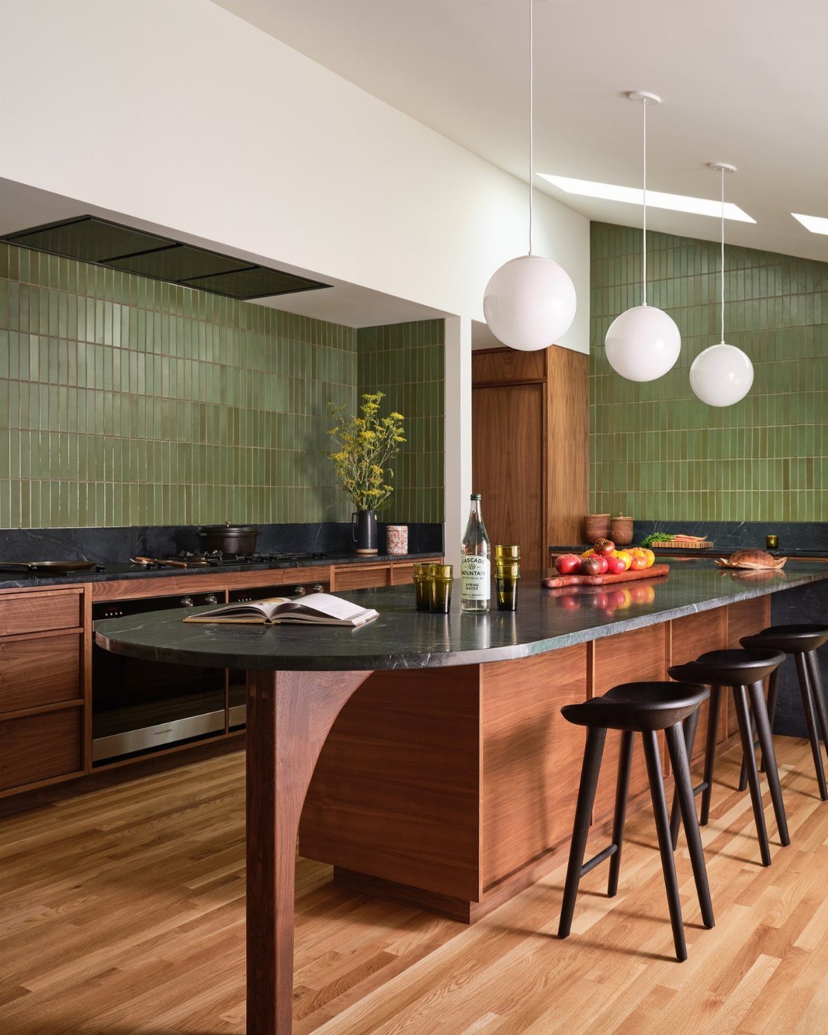Walnut wood kitchen cabinets and island with green tile backsplash and globe lights