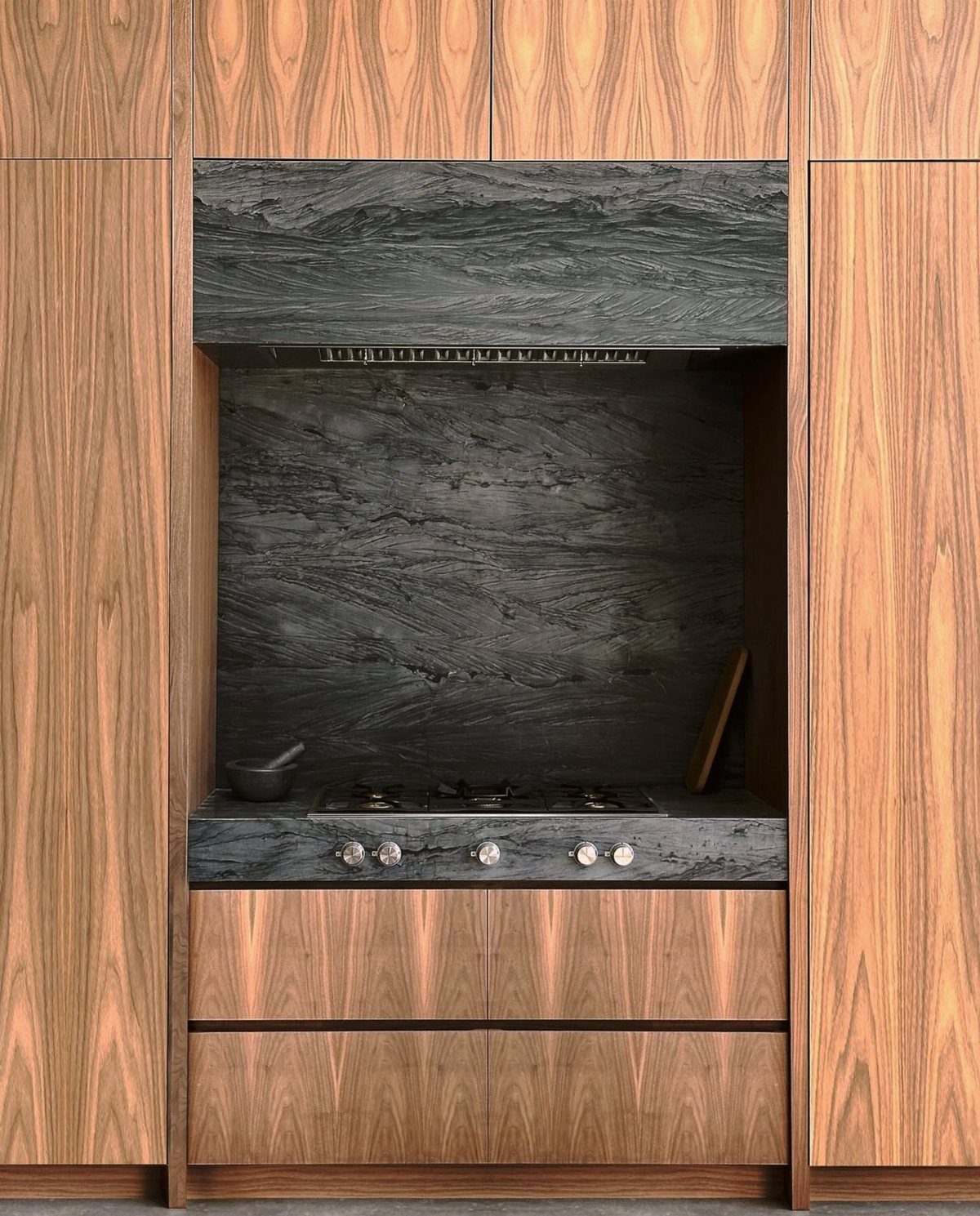 Walnut wood cabinets surrounding a dark textured black stone kitchen backsplash and countertop.
