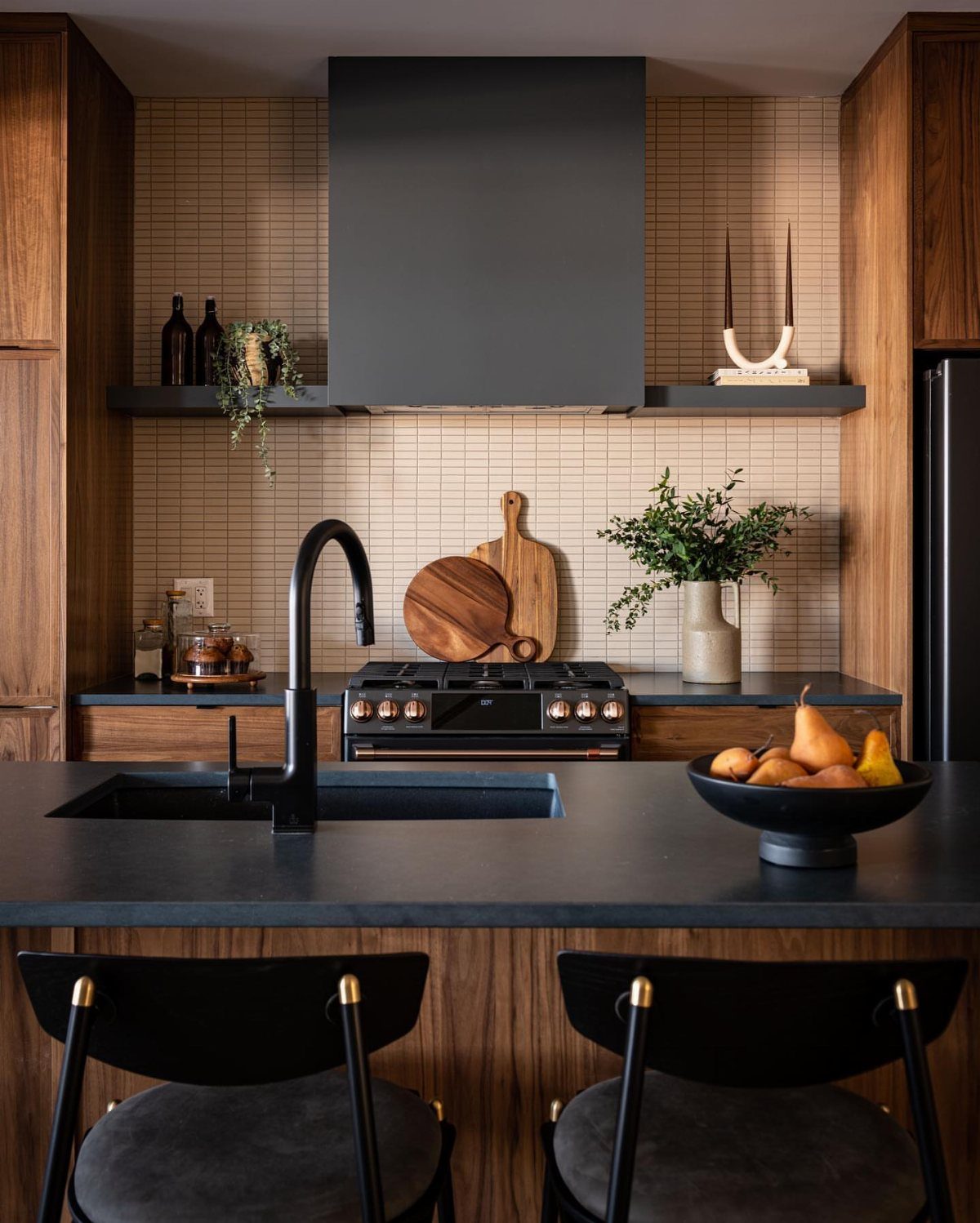 Walnut kitchen cabinets and island with dark charcoal countertops and black fixtures.