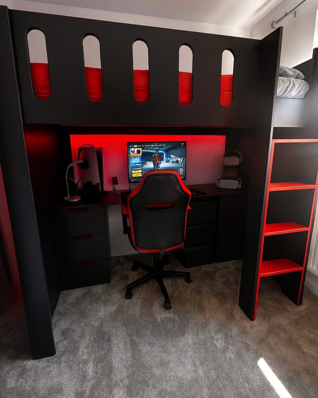 Black loft bed with red accents and a built-in gaming desk and drawers.