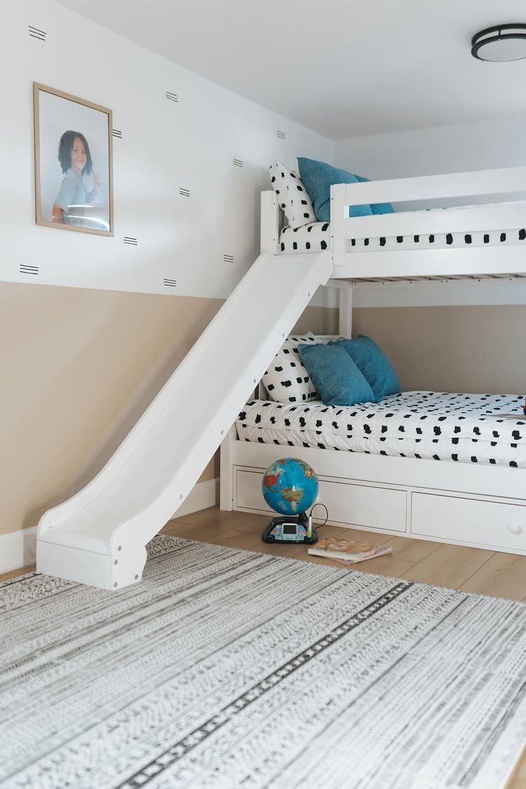 White bunk bed with a slide, polka dot bedding, and a blue globe.