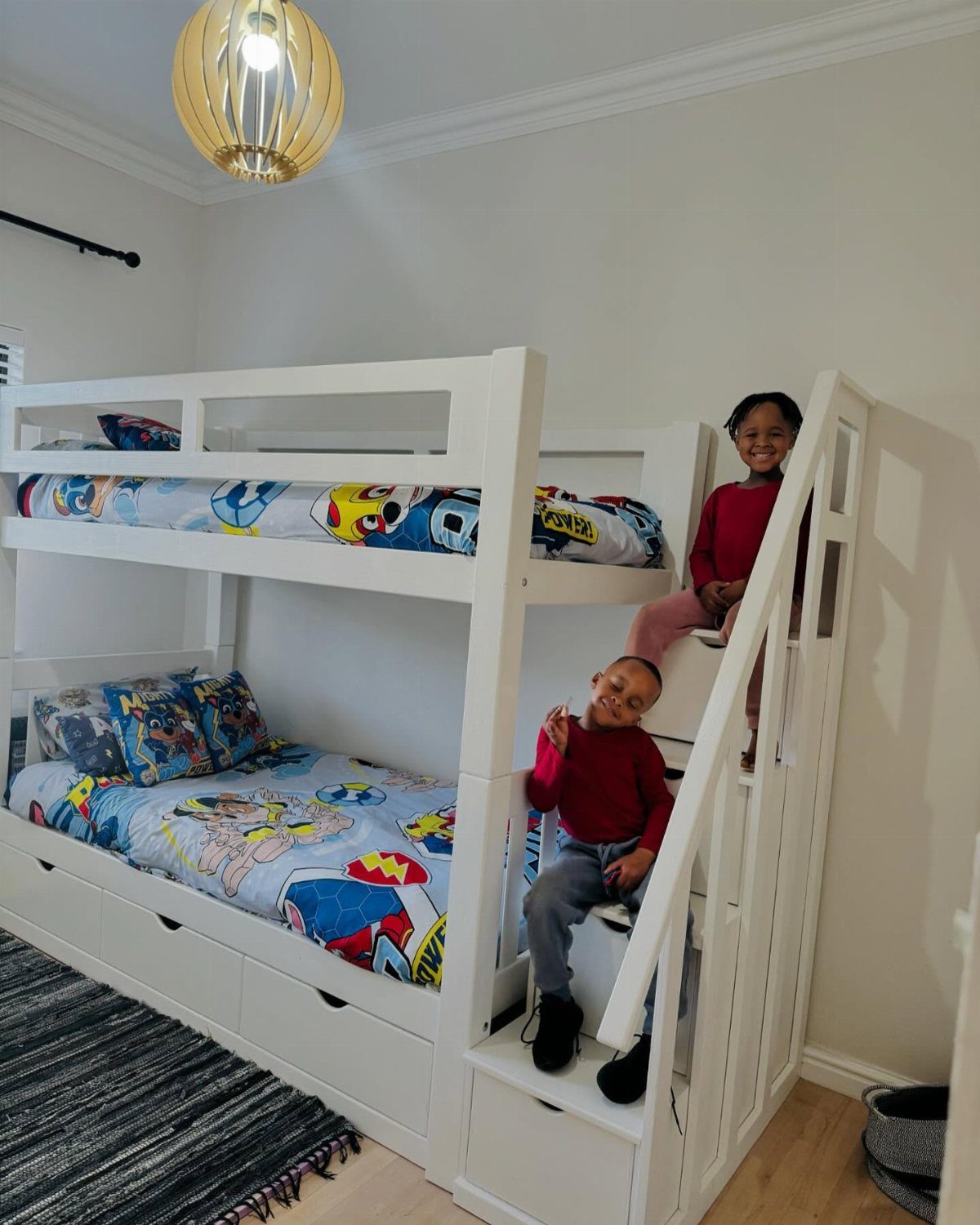White wooden bunk bed with built-in stairs and two boys sitting on it.
