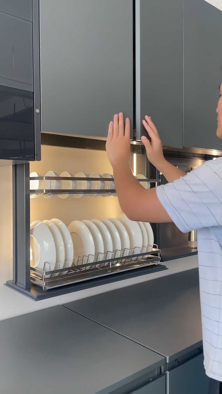 Cabinet Color Trends: 11 Ideas for Your Kitchen in 2026 8 Gray kitchen cabinets with a pull-down rack holding white ceramic plates.