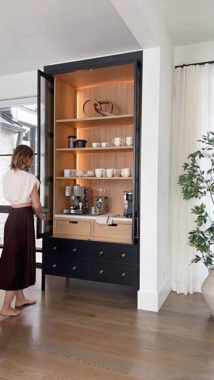 Built-in black coffee bar cabinet with wooden shelves and espresso machine in a room.
