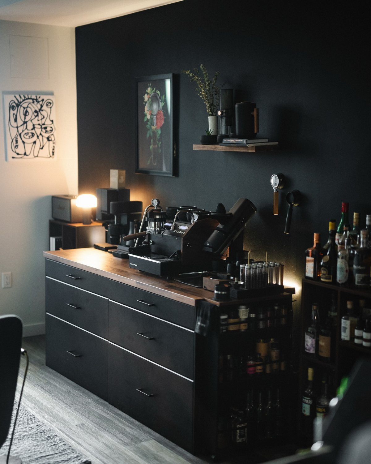 Dark coffee bar with a black espresso machine on a wooden countertop against black walls.