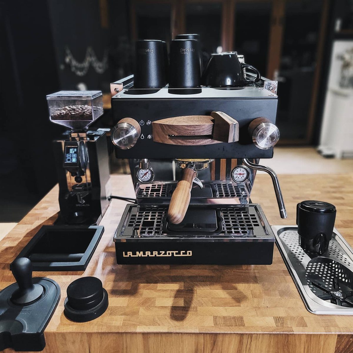 Black espresso machine and grinder on a wooden countertop with black coffee cups.