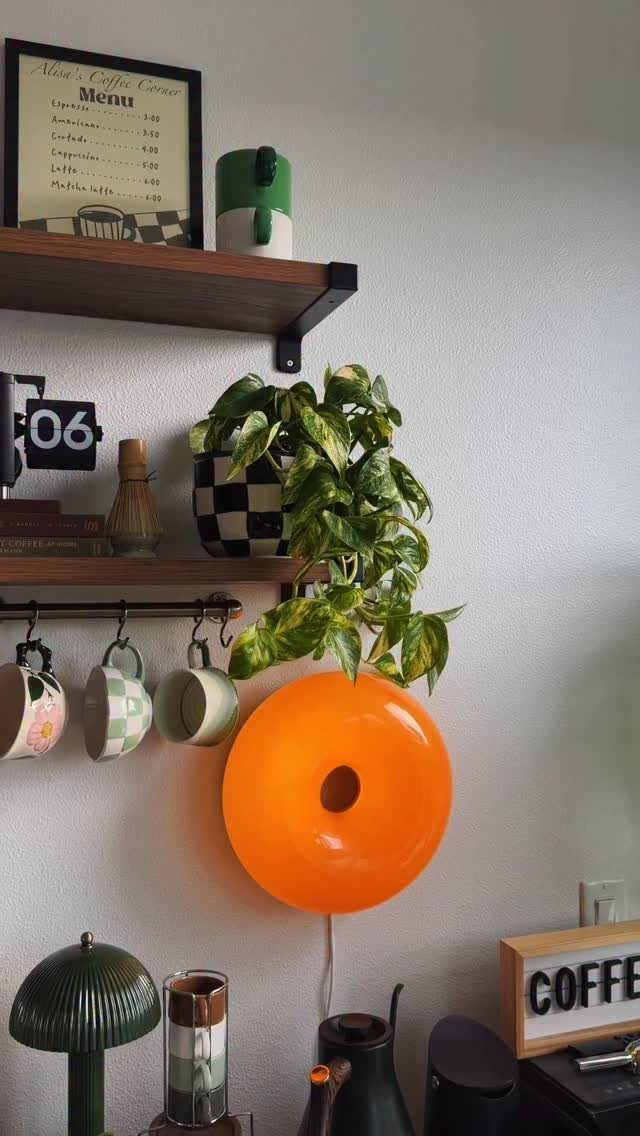 Coffee station with dark wood floating shelves, hanging mugs, and a bright orange lamp.