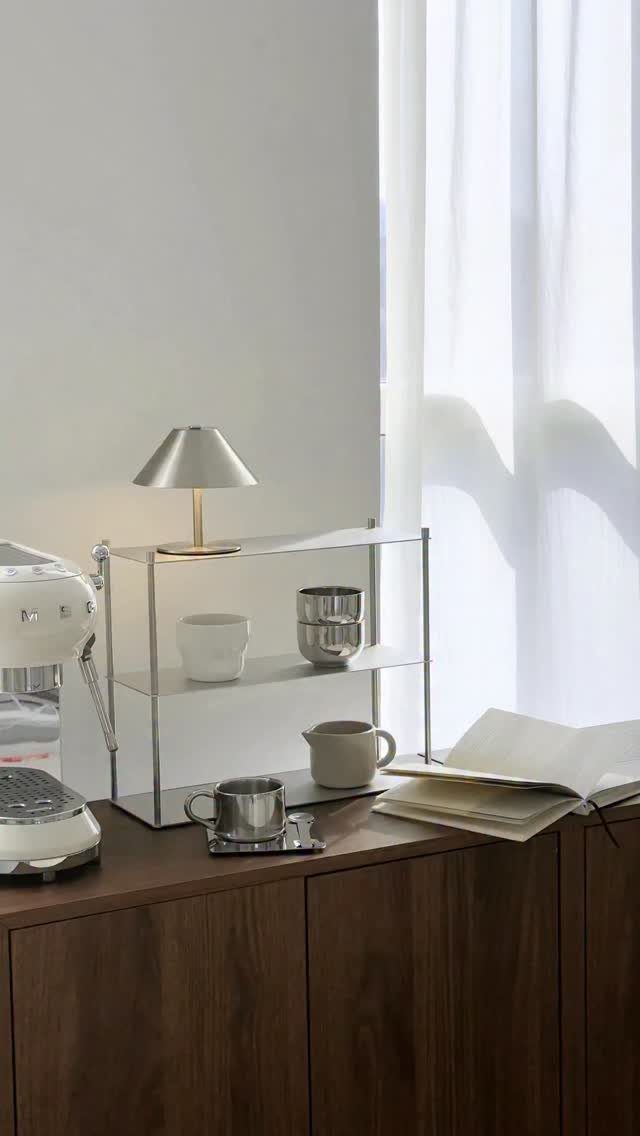 White espresso machine and silver lamp on a dark wood sideboard coffee station.