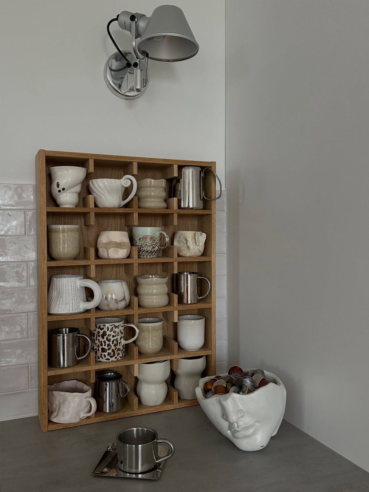 Wooden grid shelf displaying a variety of ceramic and metal coffee mugs.
