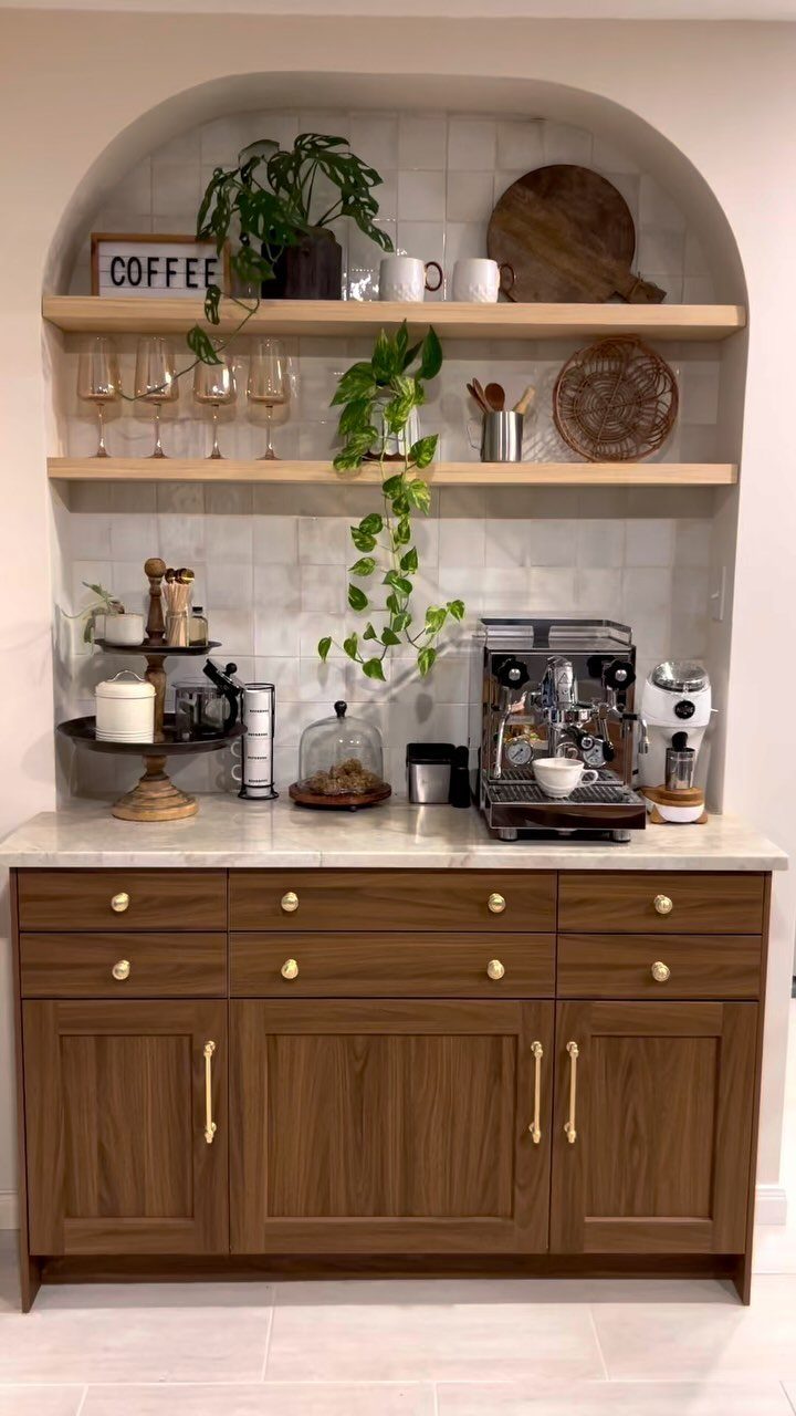Coffee station in an arched alcove with wooden cabinets and floating shelves.