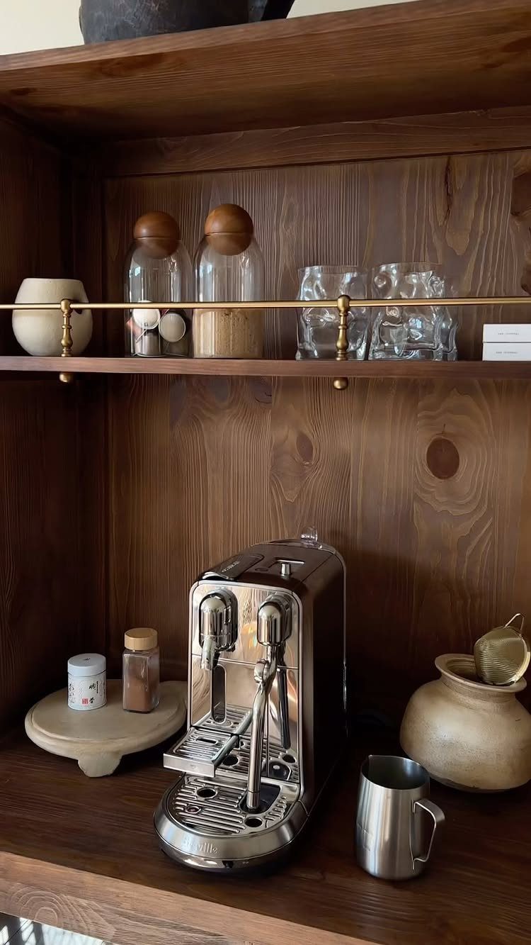 Silver espresso machine in a dark wood built-in coffee bar with glass jars.