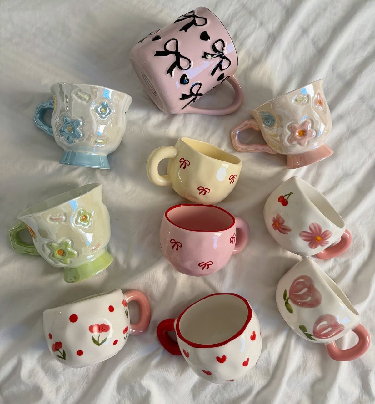 Assorted decorative ceramic mugs with floral and heart patterns on white fabric