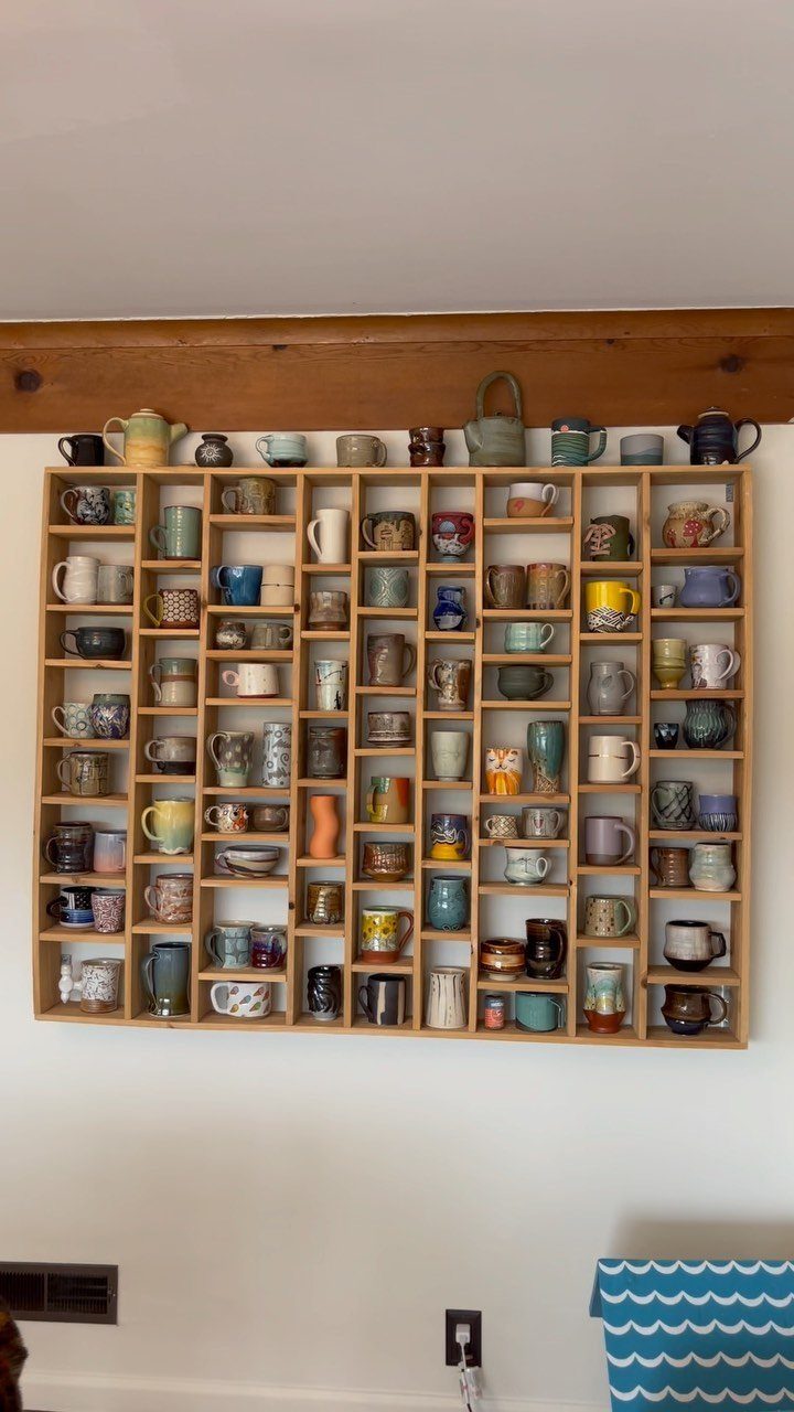 Assorted ceramic mugs of various colors and patterns displayed in a wooden grid shelf