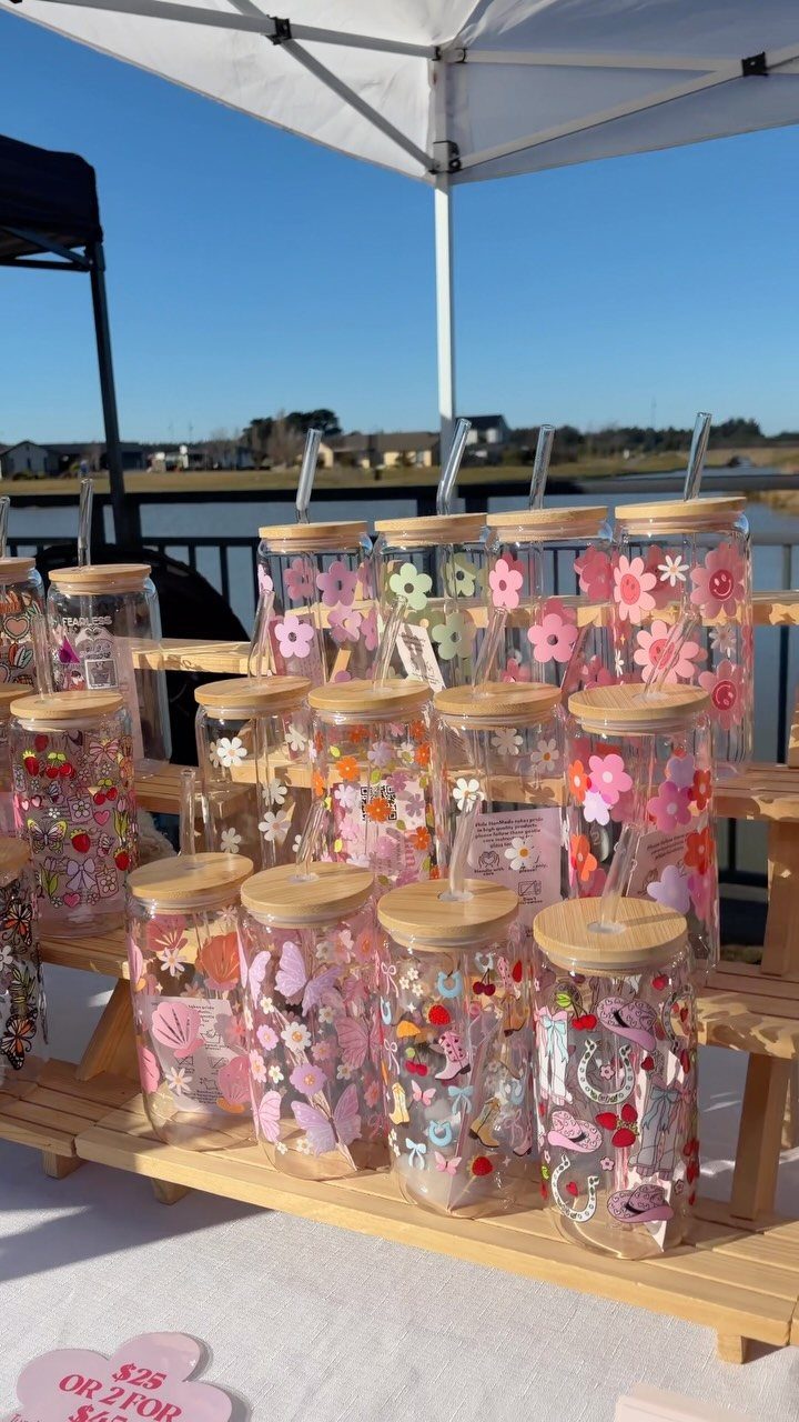 Glass cups with bamboo lids and straws decorated with colorful floral stickers on wooden shelves.