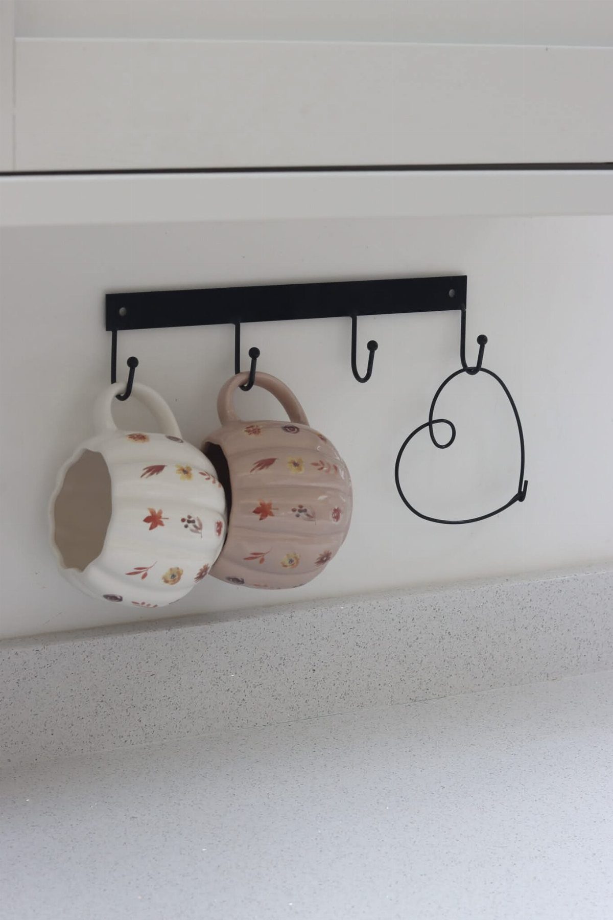 Two floral ceramic mugs hanging from a black metal rail with hooks.