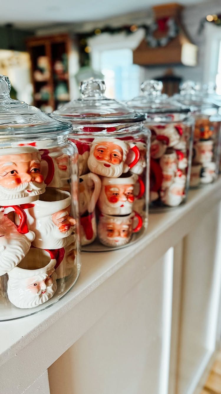 Santa Claus face ceramic mugs stored inside clear glass jars on a white shelf.