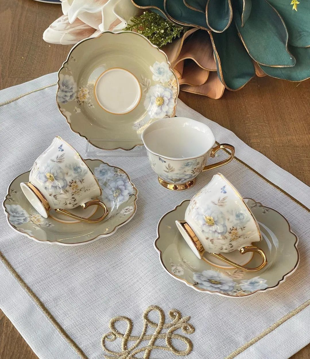 White porcelain teacups with blue floral patterns and gold rims on scalloped saucers.