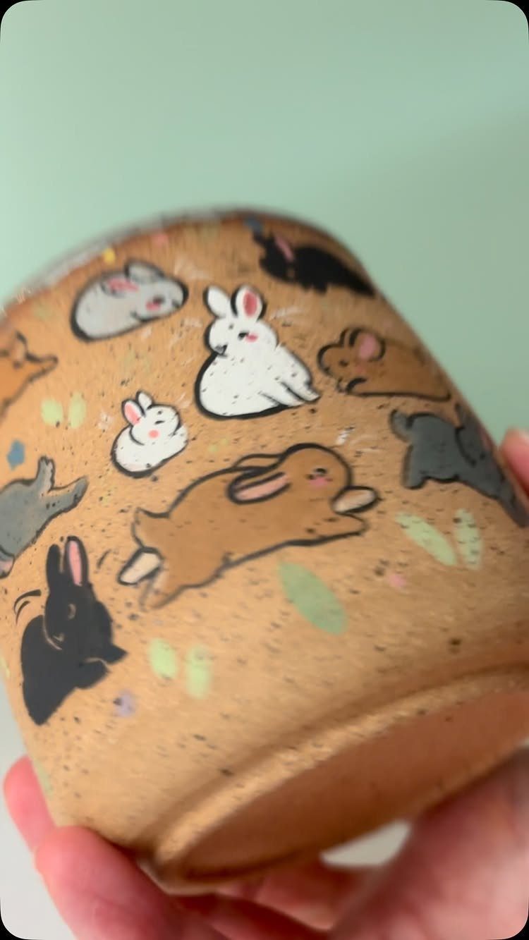 Beige ceramic mug with a pattern of small illustrated rabbits in various colors.