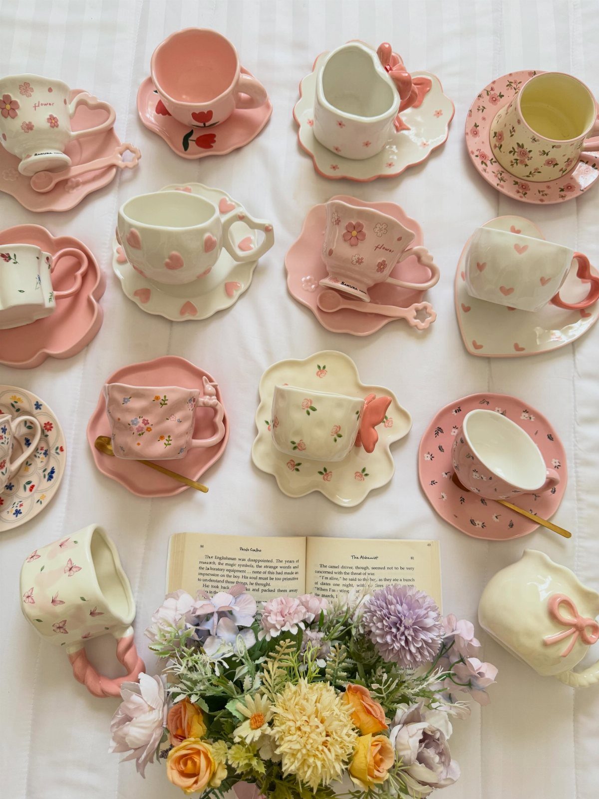 Pastel ceramic tea cups with floral patterns and matching saucers on white fabric.