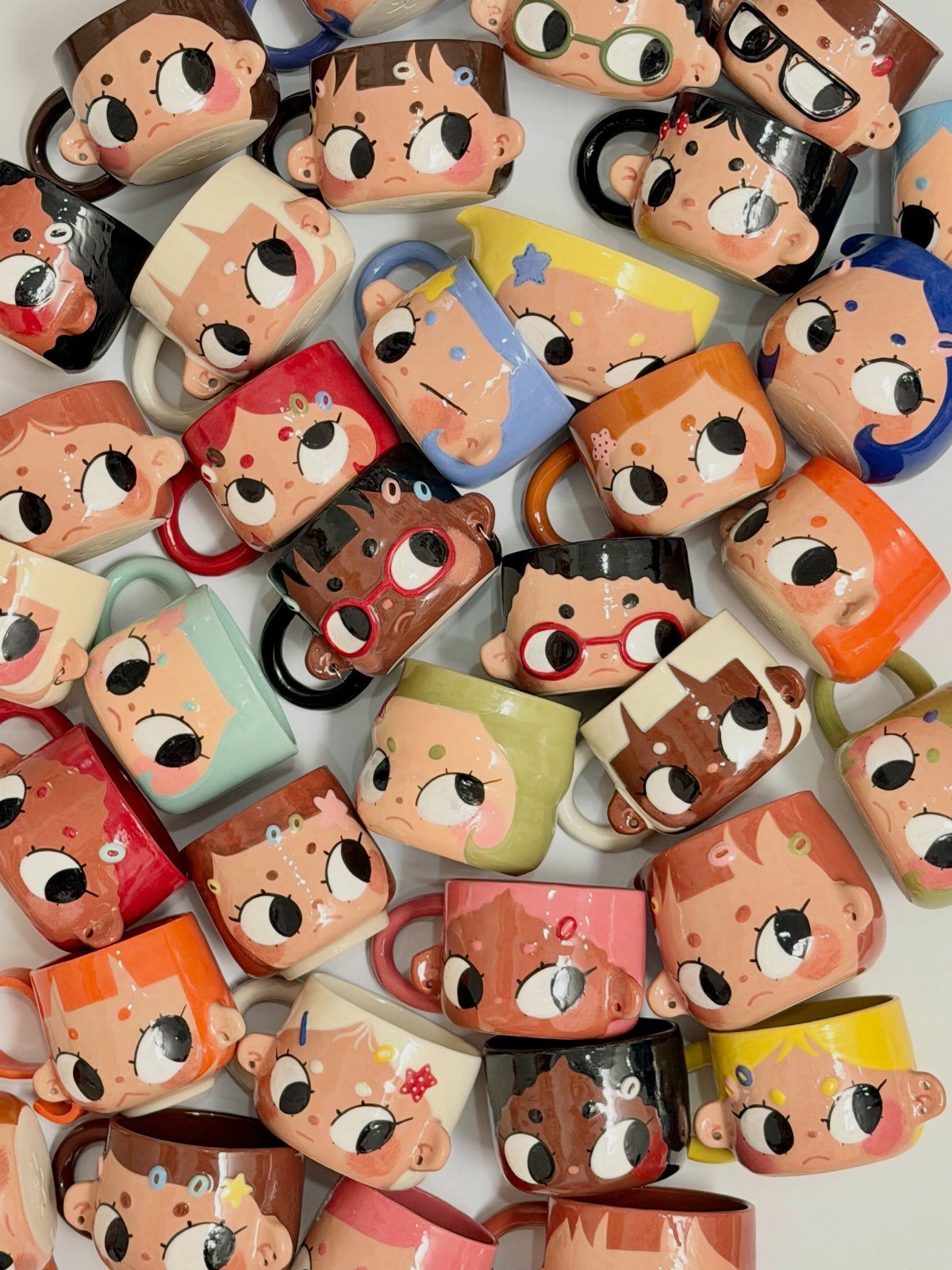Colorful ceramic mugs with stylized cartoon faces scattered on a white background.