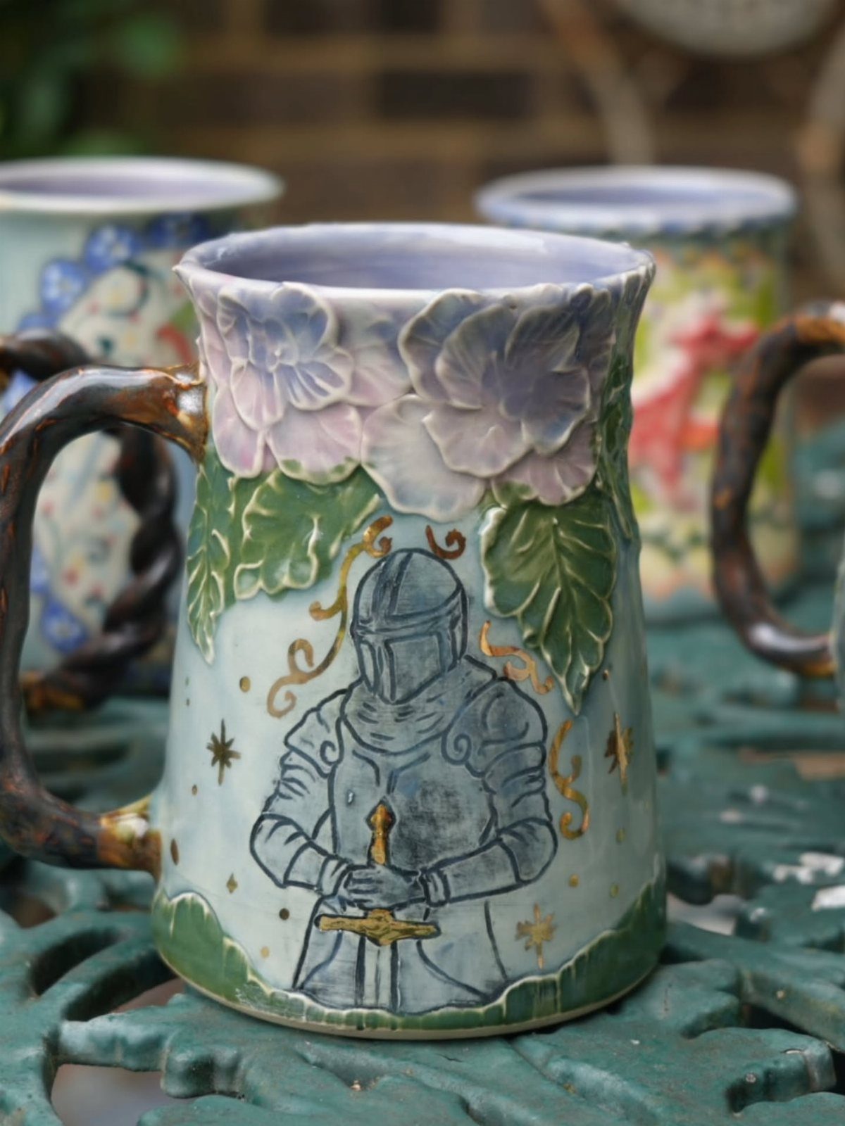Ceramic mug featuring a painted knight and sculpted purple flowers on a garden table