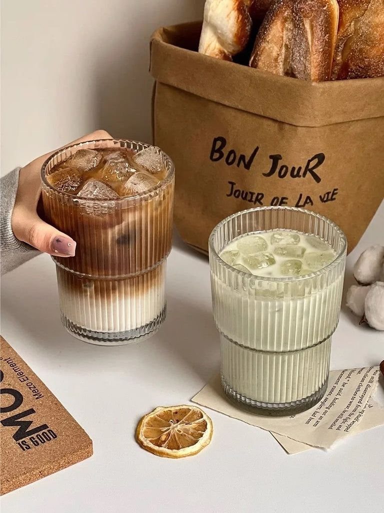 Two ribbed glass mugs with iced drinks next to a bag of bread.