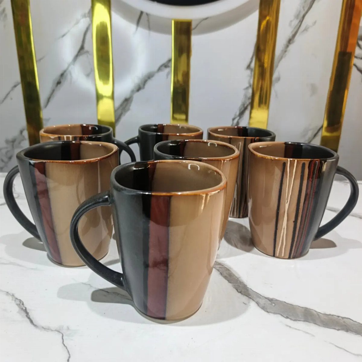 Brown and black striped ceramic mugs arranged on a white marble surface.