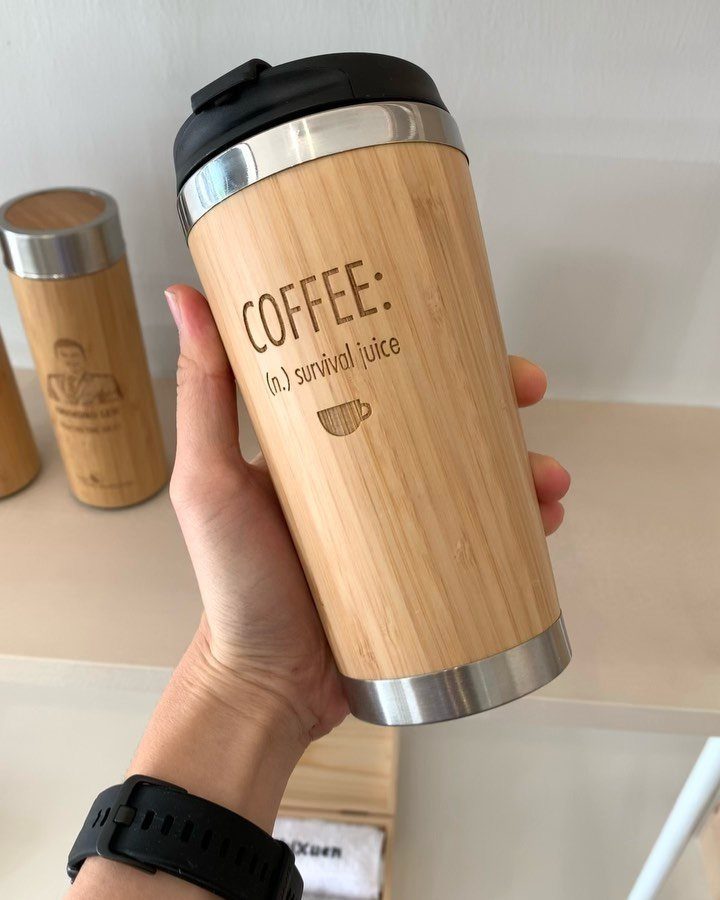 Bamboo travel mug with coffee survival juice text held in a person's hand.